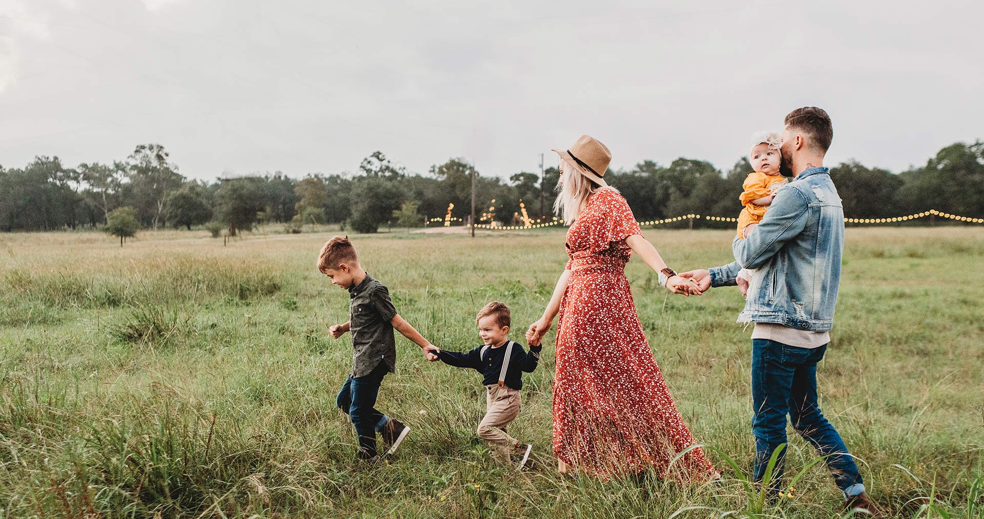 two young children, a woman, and a man holding a baby walking hand in hand in a field